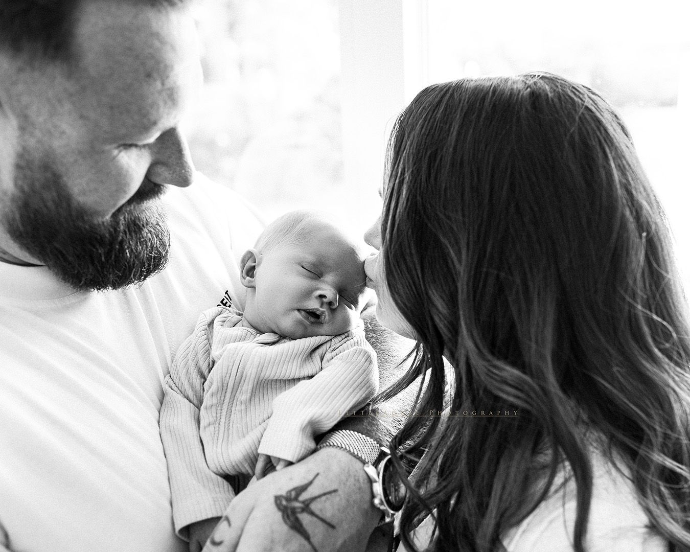A couple gently holds their newborn baby together in an intimate black and white portrait.