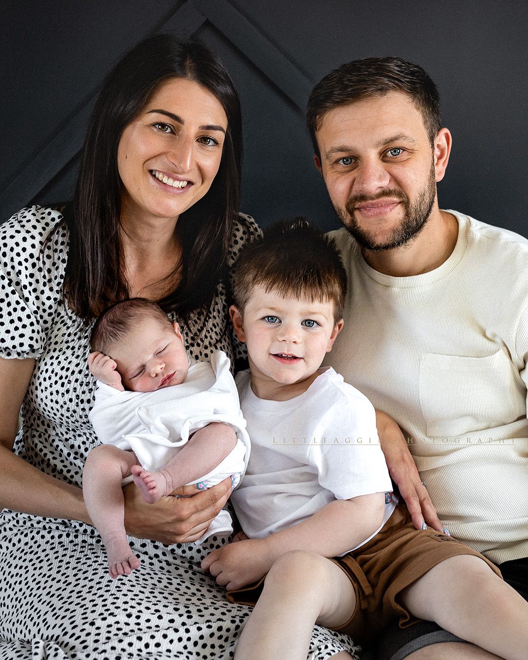 Family in white and polka dot attire sitting together on sofa in lifestyle photo session.