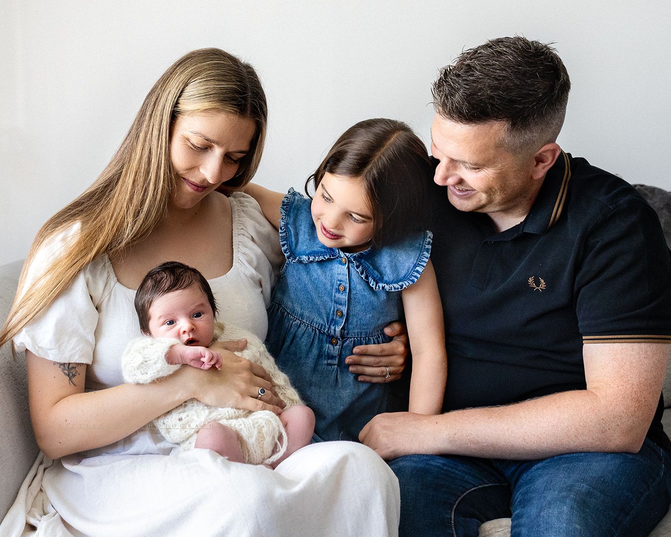 A happy family of four admiring their newborn baby, posing together for a professional portrait photo.
