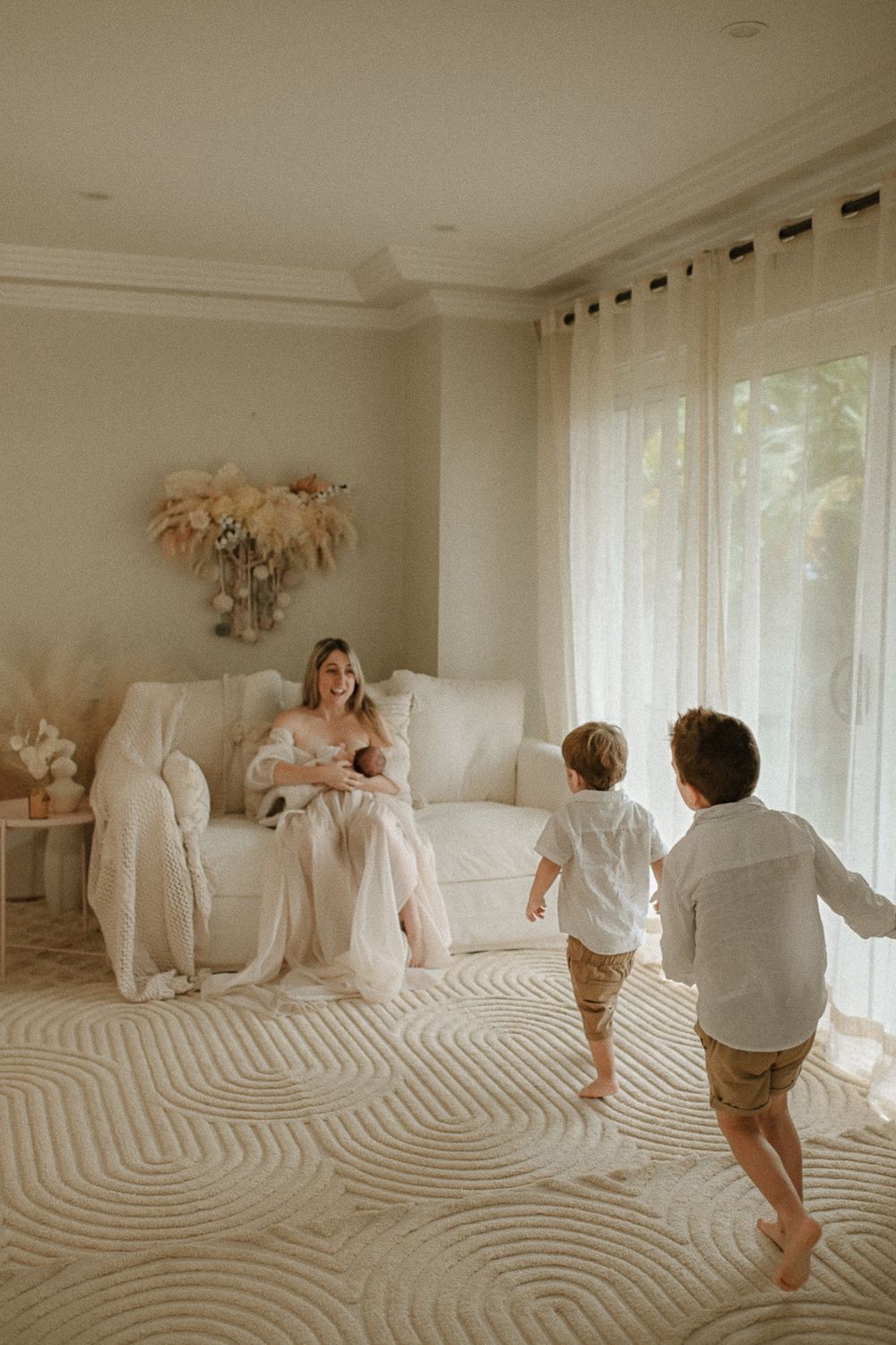 Children run excitedly across a patterned carpet towards a figure seated on a white couch.