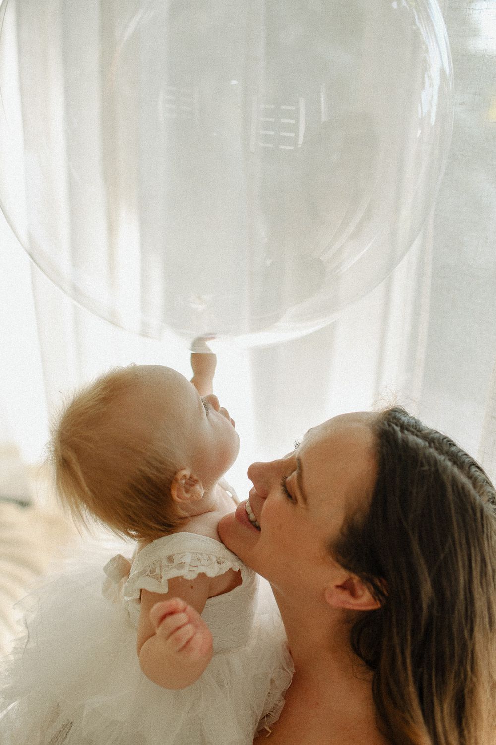 An intimate indoor portrait with soft natural lighting through sheer curtains.