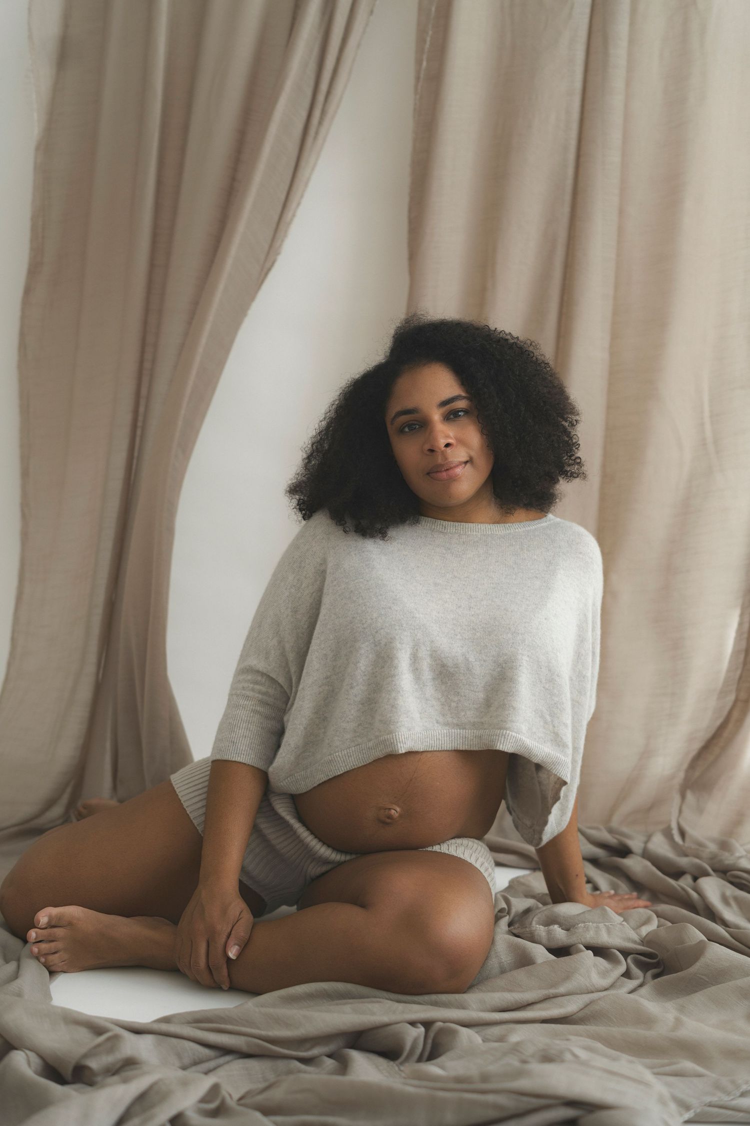Maternity portrait of expecting mother in casual attire sitting on beige bedding.