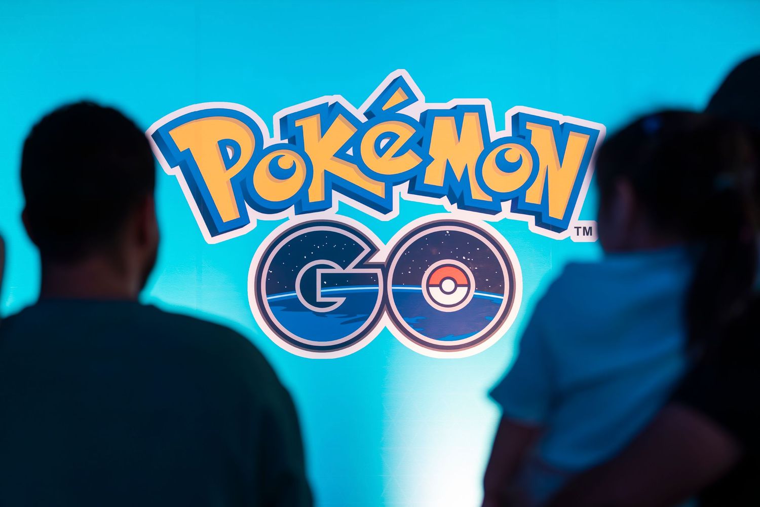 Pokemon GO mobile game logo displayed on bright blue screen with silhouetted figures in foreground.