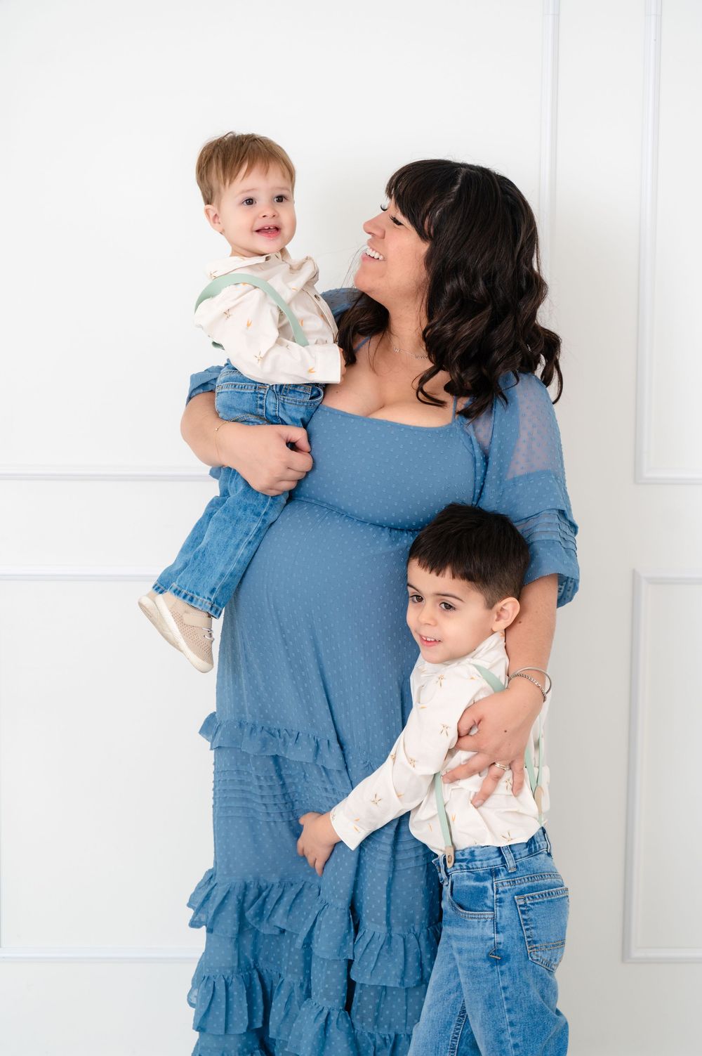 Family wearing coordinated blue outfits embraces and laughs together against a white wall.