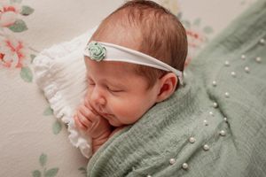 Newborn baby sleeping peacefully on sage green textured blanket.