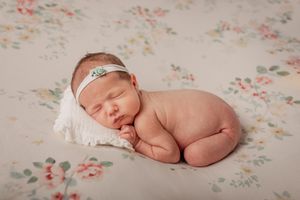 Sleeping newborn on floral pattern blanket with delicate headband.