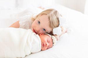 Baby lying on white blanket with soft natural lighting.