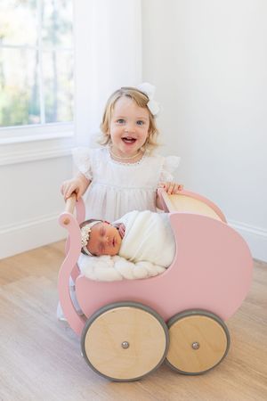 Child playing with pink vintage toy pram on hardwood floor.