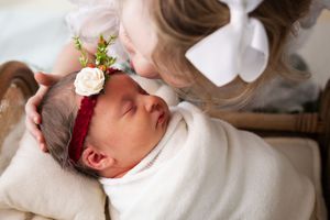 Toddler and newborn sibling sharing tender moment on white blanket.
