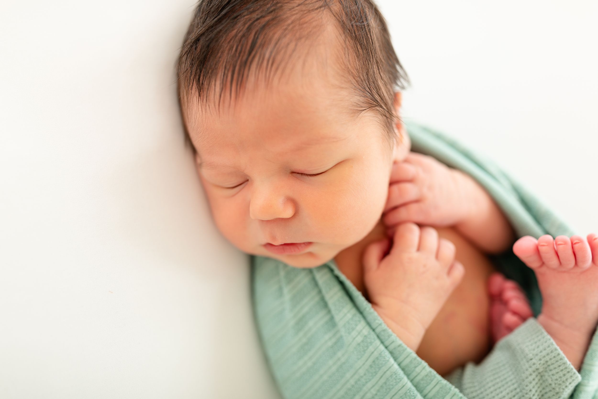 Artistic newborn photography in mint green tones capturing peaceful sleeping moments.