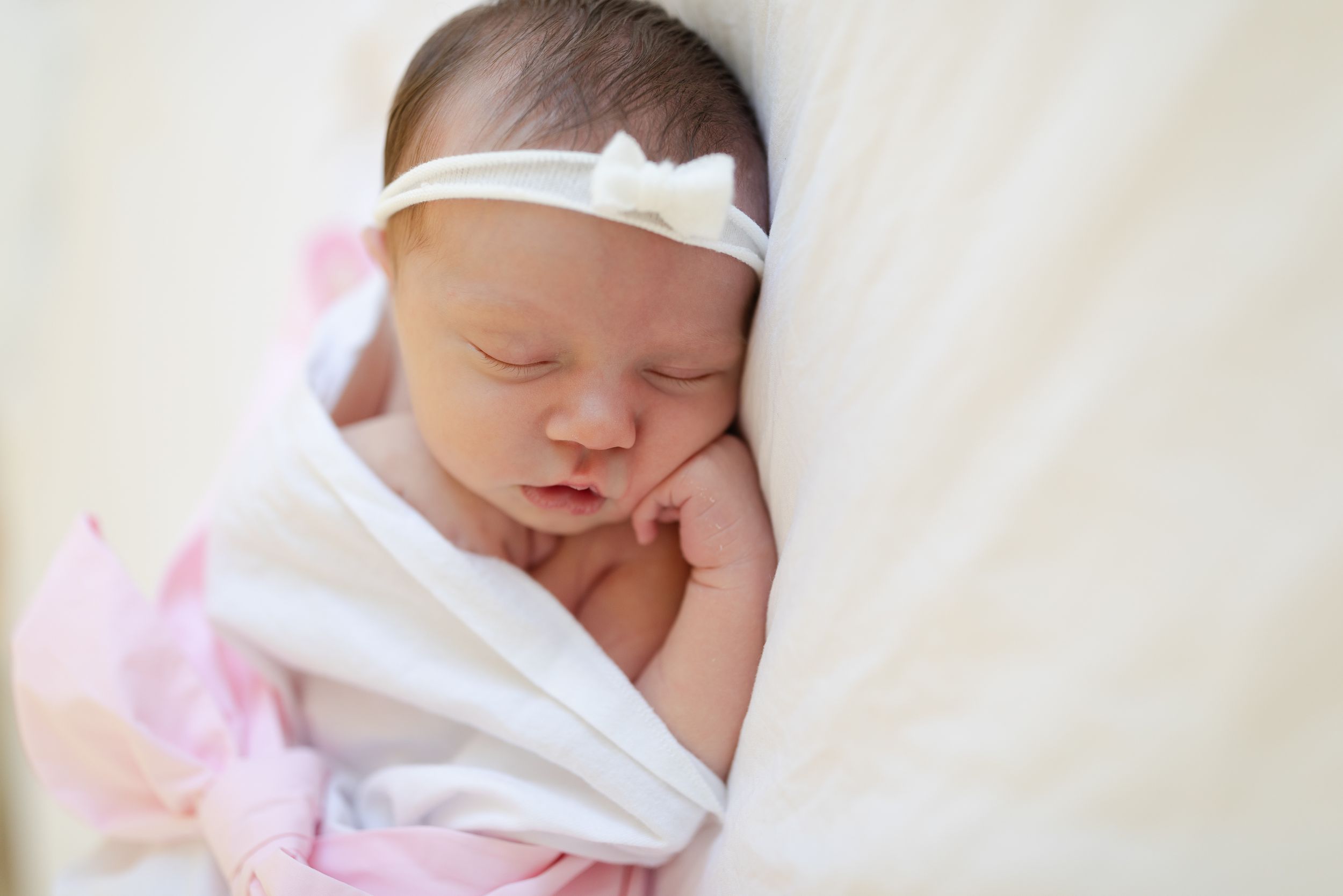 Sleeping newborn baby wrapped in white blanket on soft bedding.
