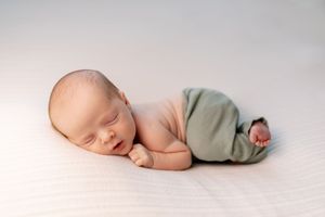 Sleeping newborn baby posed on soft white backdrop.