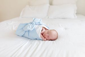 Sleeping newborn baby wrapped in soft blue blanket on white bedding.