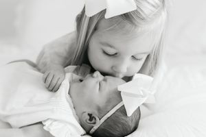 A tender black and white photograph shows a gentle moment between siblings sharing a loving kiss.