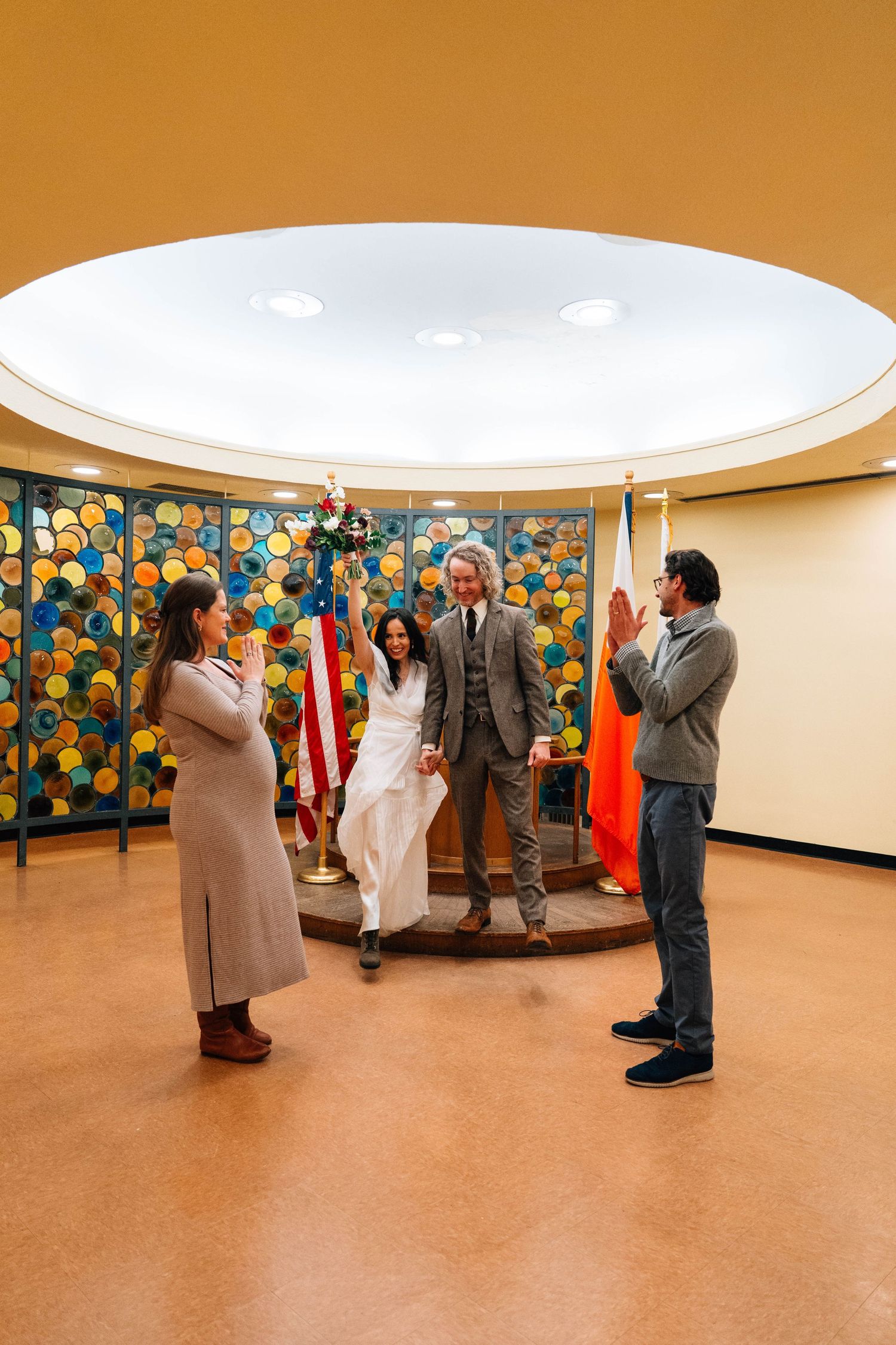 The image shows a wedding ceremony taking place in a room with colorful floral decorations on the walls.