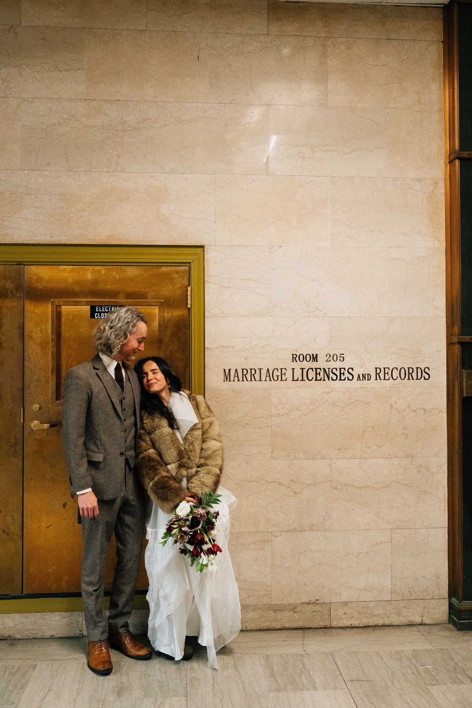 A couple stands in front of a building with a sign for marriage licenses and records.