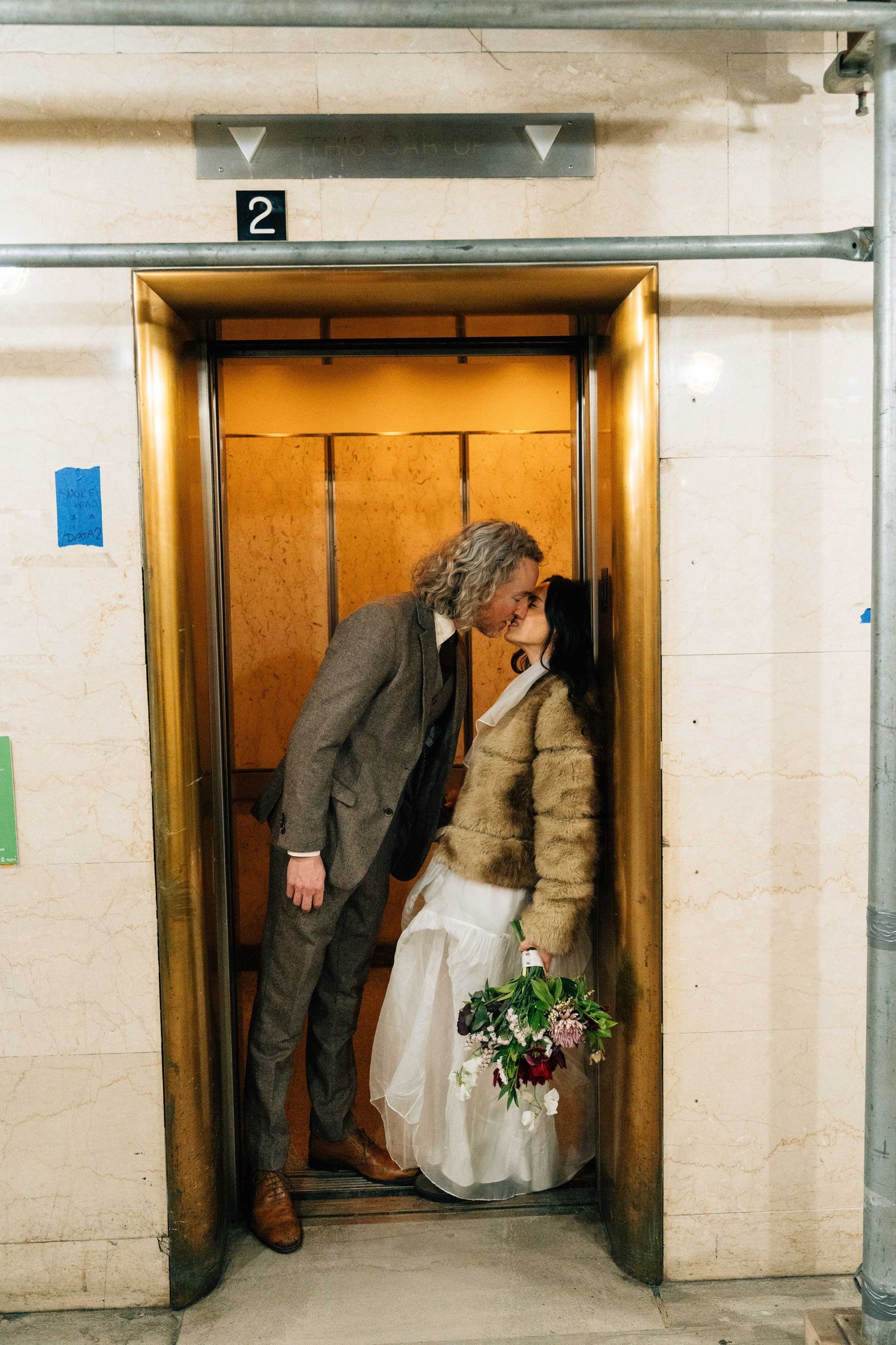 A bride and groom stand in a doorway, the bride holding a bouquet of flowers.