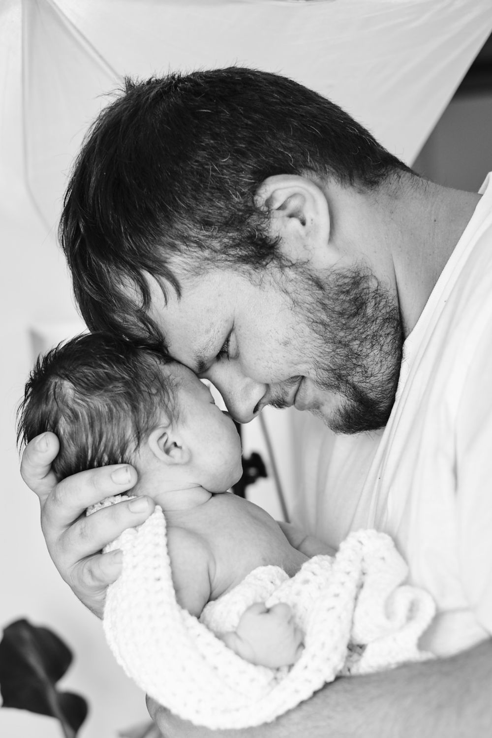 A tender black and white moment between parent and newborn wrapped in a blanket.
