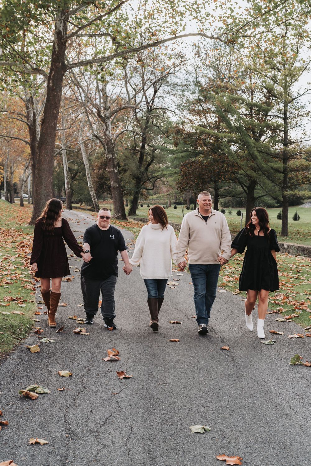A group walking together on a leaf-covered path in an autumn park setting.