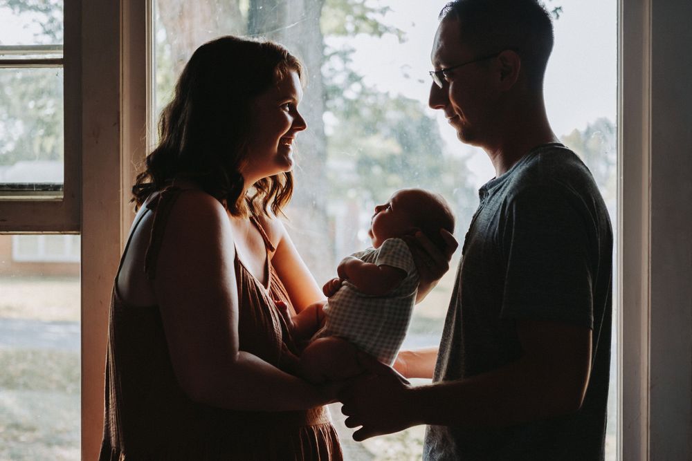 Silhouetted figures share an intimate moment by a window with soft lighting.
