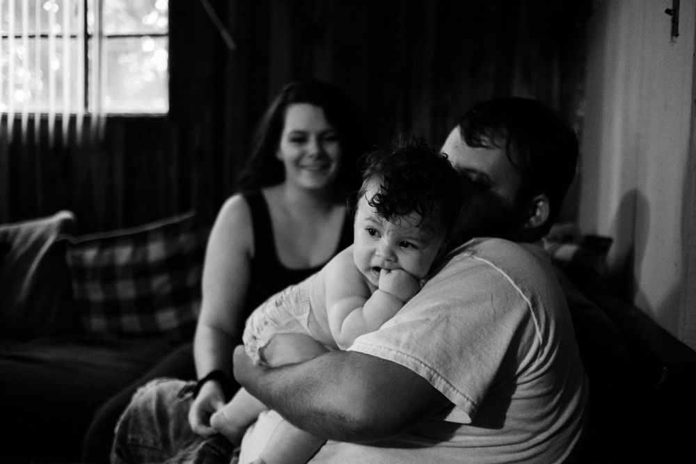 Black and white photo of intimate family moment on couch showing affection and laughter.