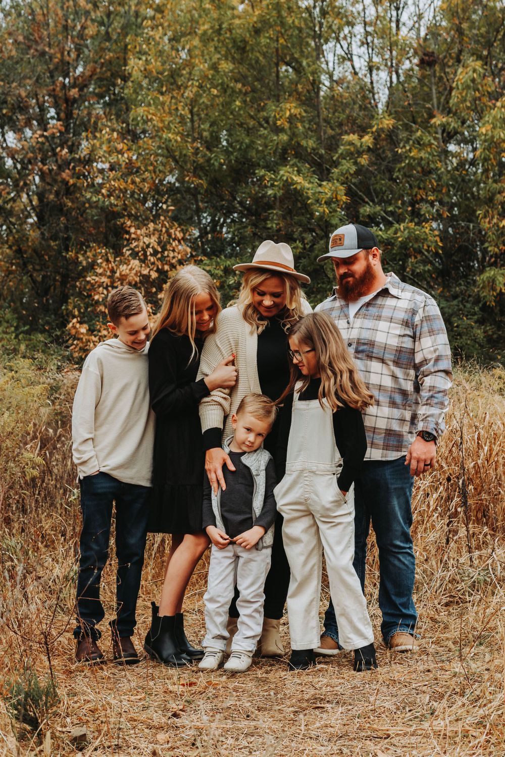 A family group poses together in casual attire against a backdrop of fall foliage.