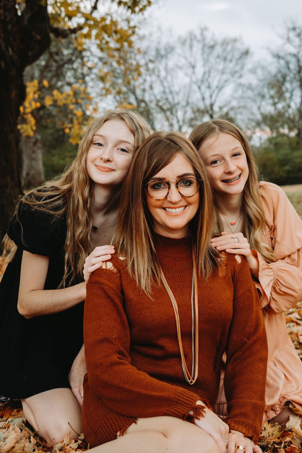 Three people pose together on fallen autumn leaves during an outdoor photo session.