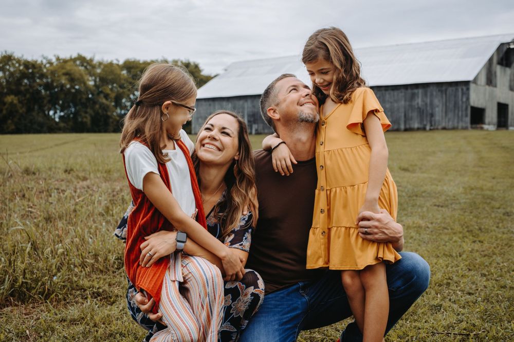 A joyful outdoor family portrait in a field with a rustic barn in the background.