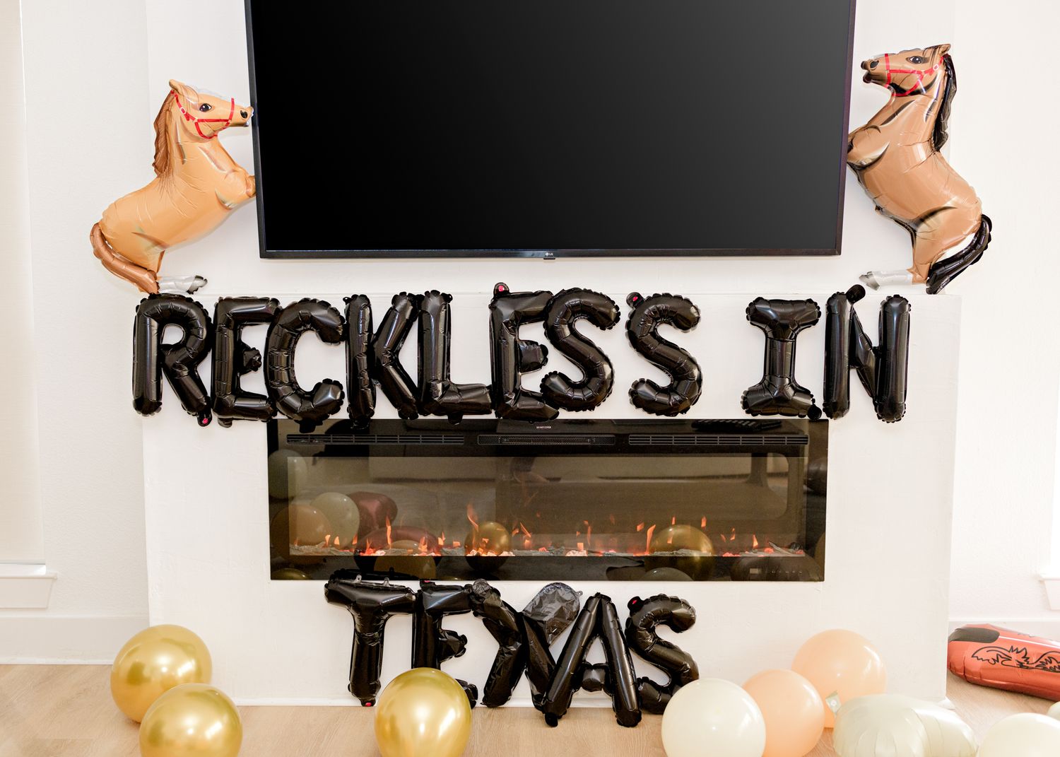 Black balloon letters spelling 'Reckless in Texas' displayed over fireplace with TV mounted above.
