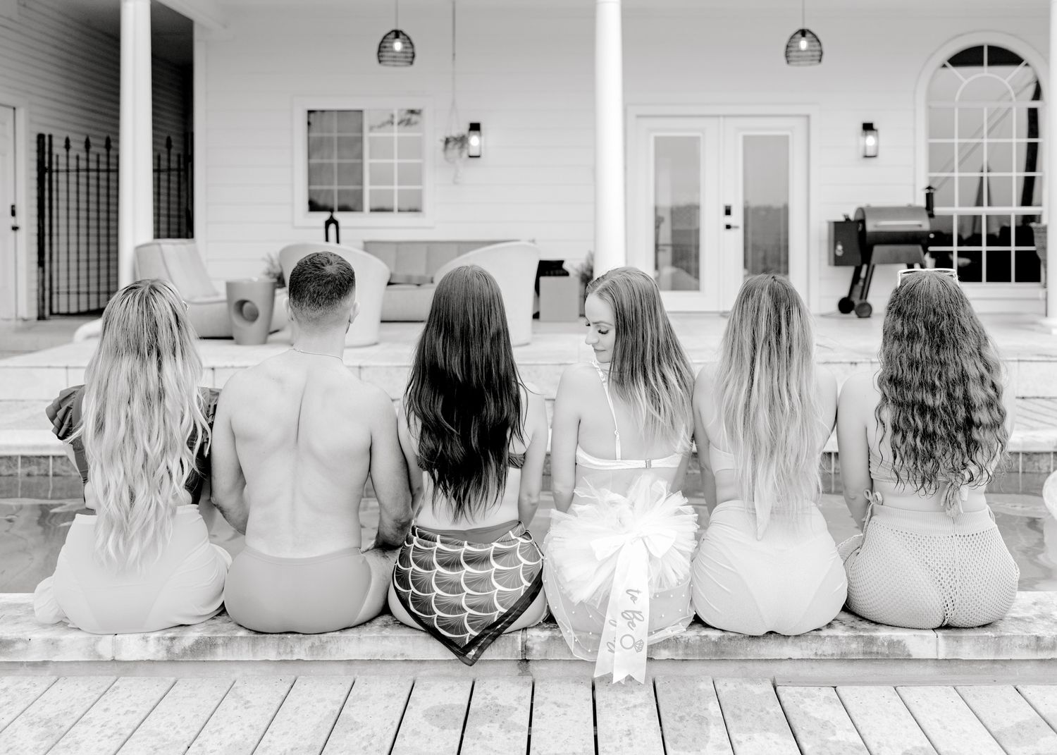 Black and white photo of friends sitting together on a white deck.