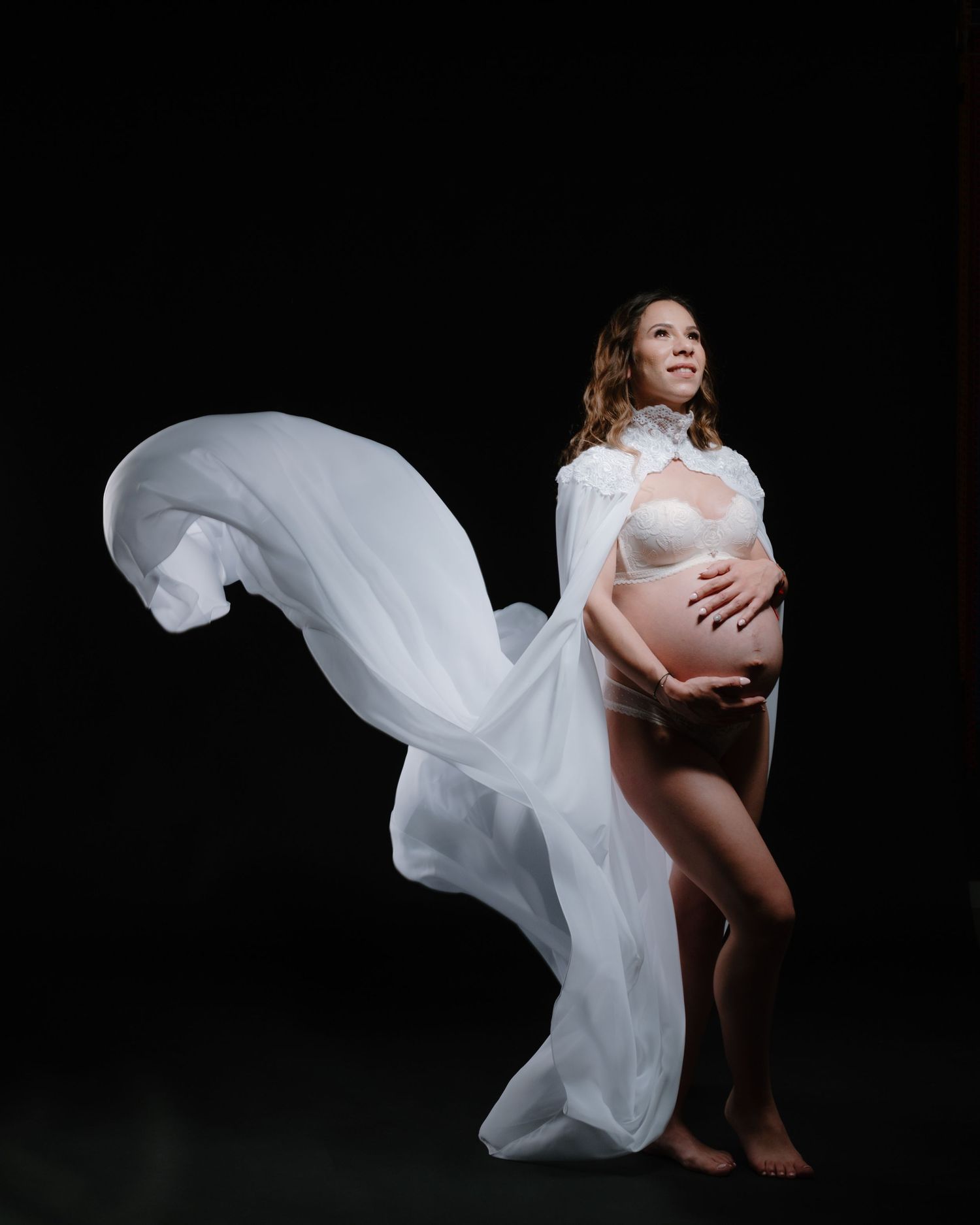 Artistic maternity photo with flowing white fabric against black background.