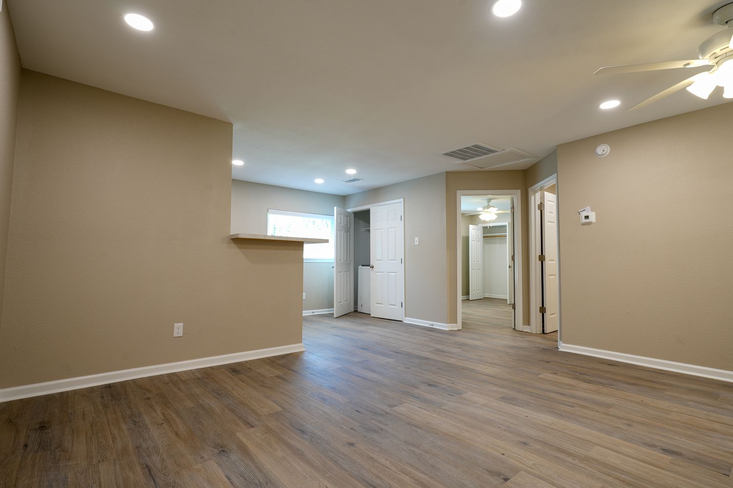 Empty living room interior with wood flooring, recessed lighting, and beige walls.