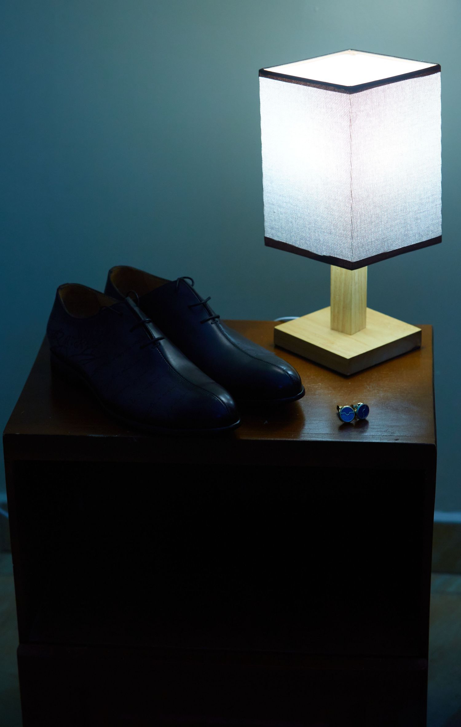 A modern table lamp with white square shade and wooden base sits on a dark surface.