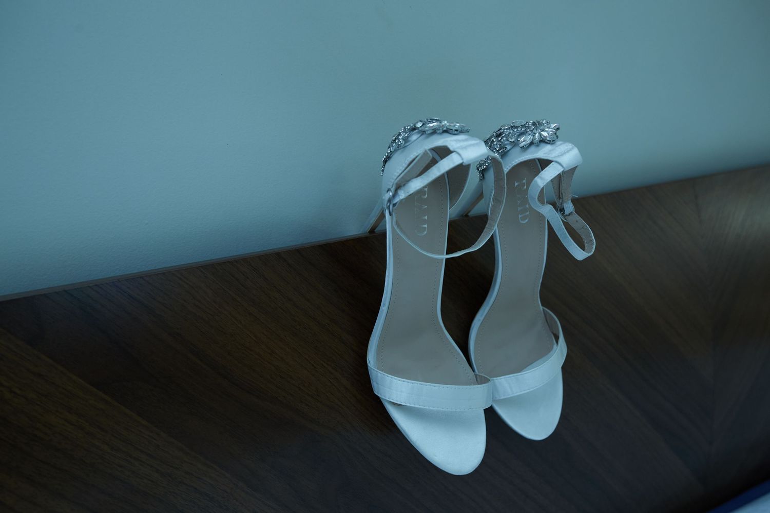 White wedding shoes with decorative details displayed on a dark wooden surface.