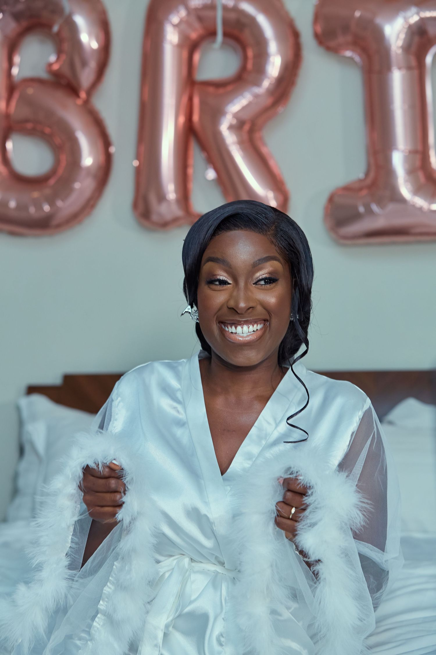 Wedding preparation scene with white satin robe and rose gold balloon decorations.