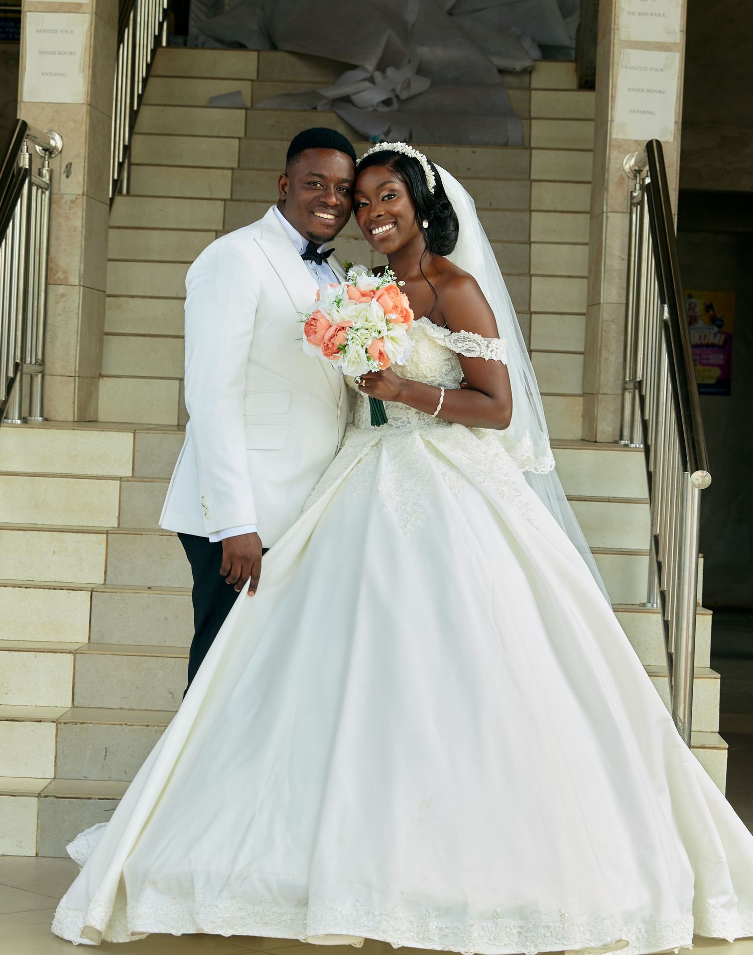 Newlyweds share joyful moments on architectural steps in traditional wedding attire.