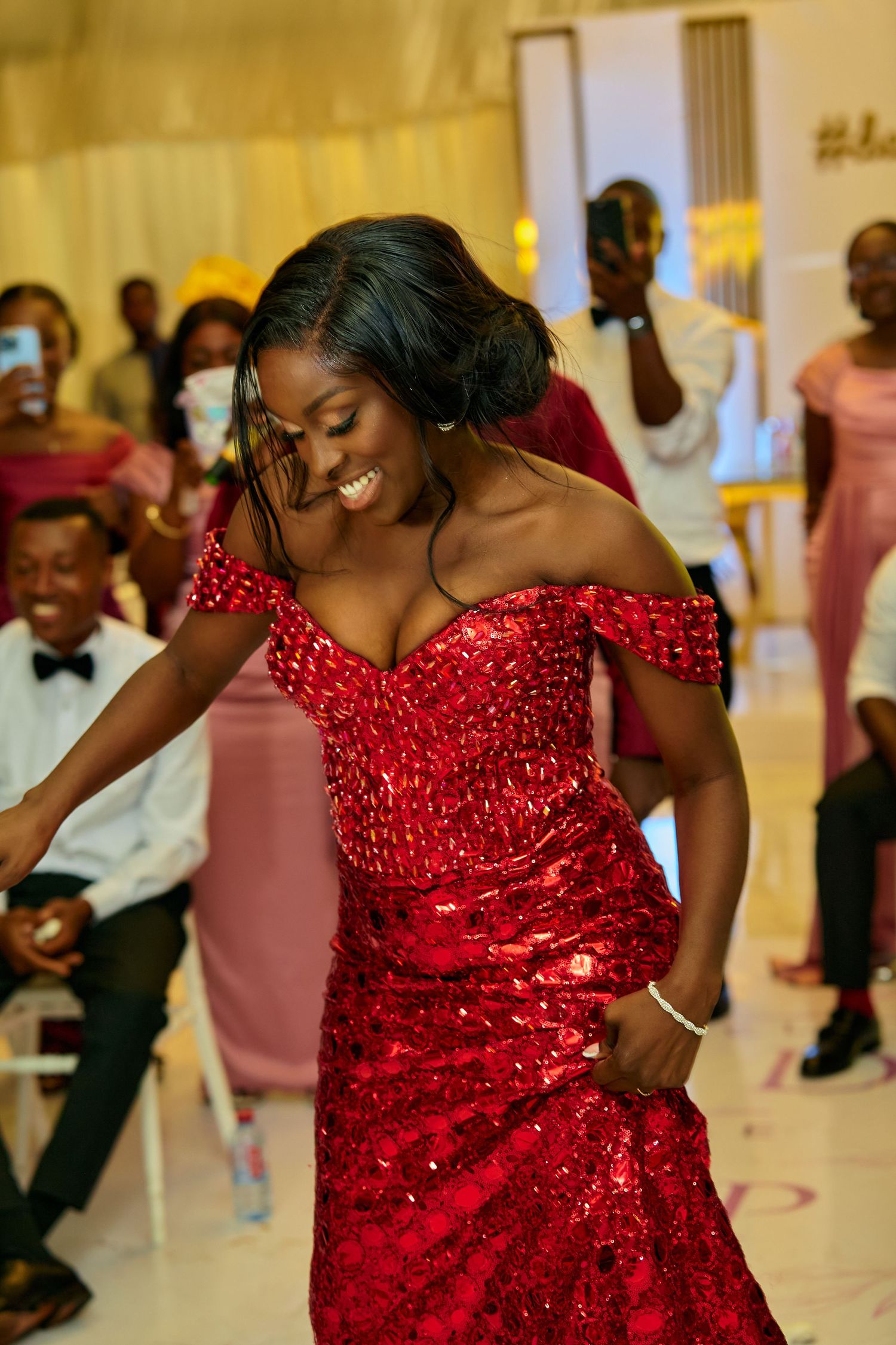 Woman in sparkling red dress dances energetically at wedding reception.
