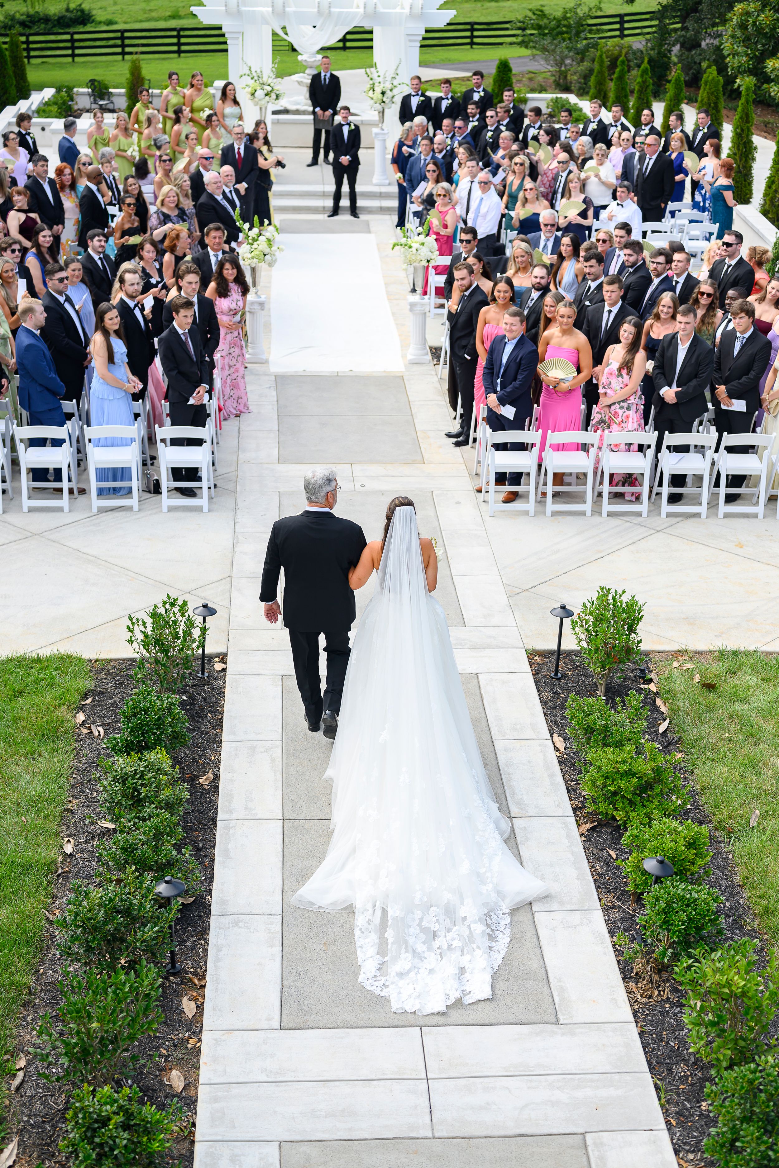 Aerial view of bride walking down the aisle with her father at an elegant outdoor wedding ceremony.