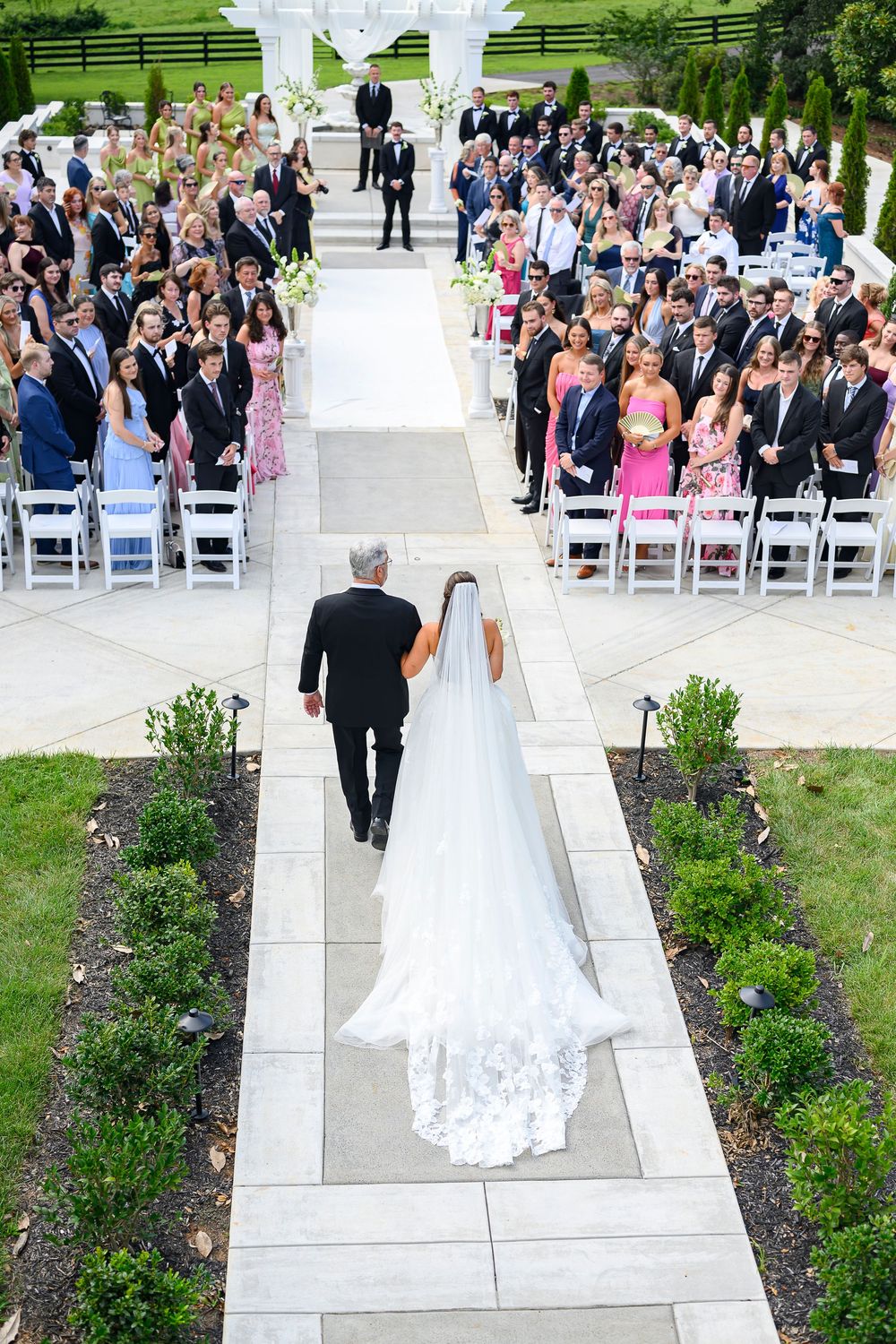 Aerial view of bride walking down the aisle with her father at an elegant outdoor wedding ceremony.