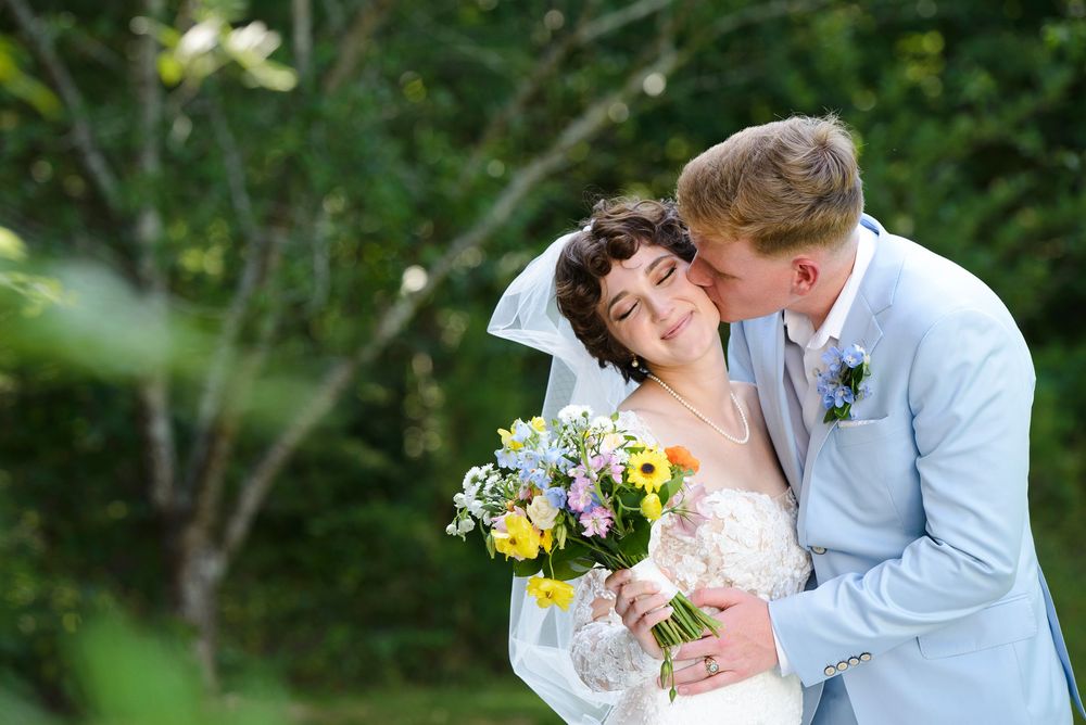 A romantic outdoor wedding scene with a couple embracing among lush greenery and summer flowers.