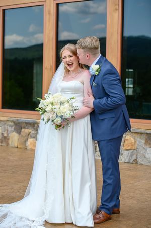 A joyful wedding couple shares a candid moment outside a venue with stone walls and large windows in the background. Talking rock, georgia