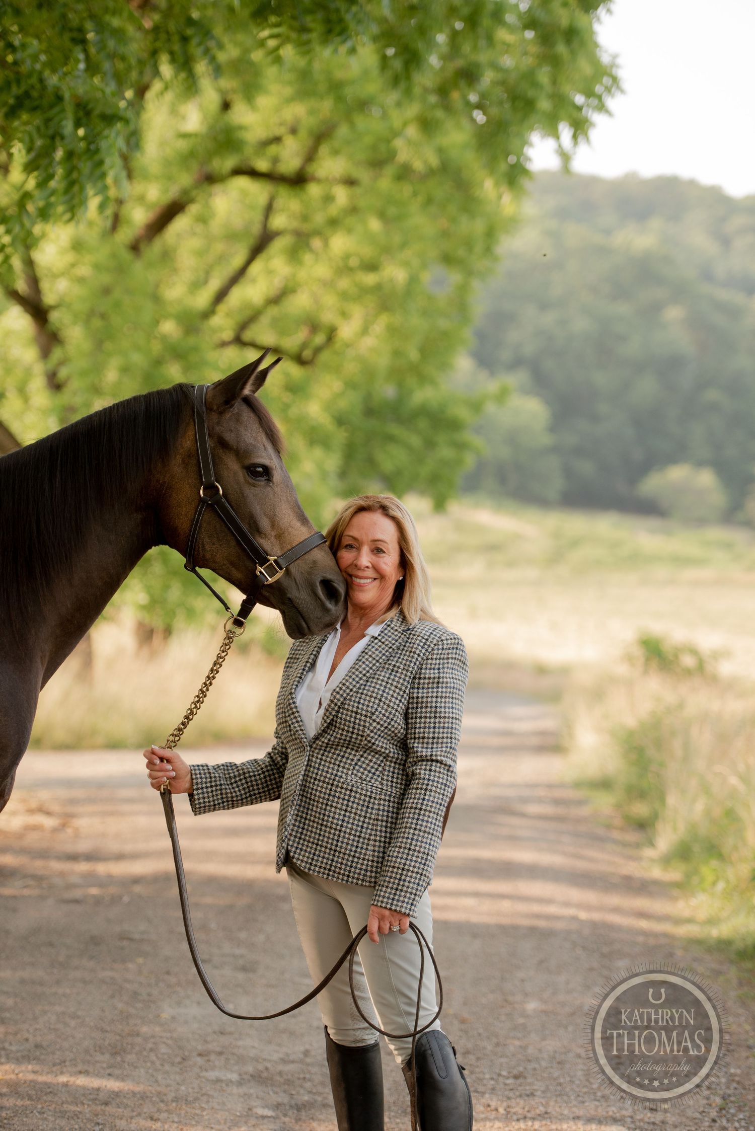 Well-groomed horse and handler pose together on a tree-lined path in afternoon light.