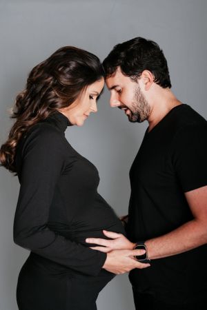 Intimate couples maternity photoshoot with both wearing black against gray background.