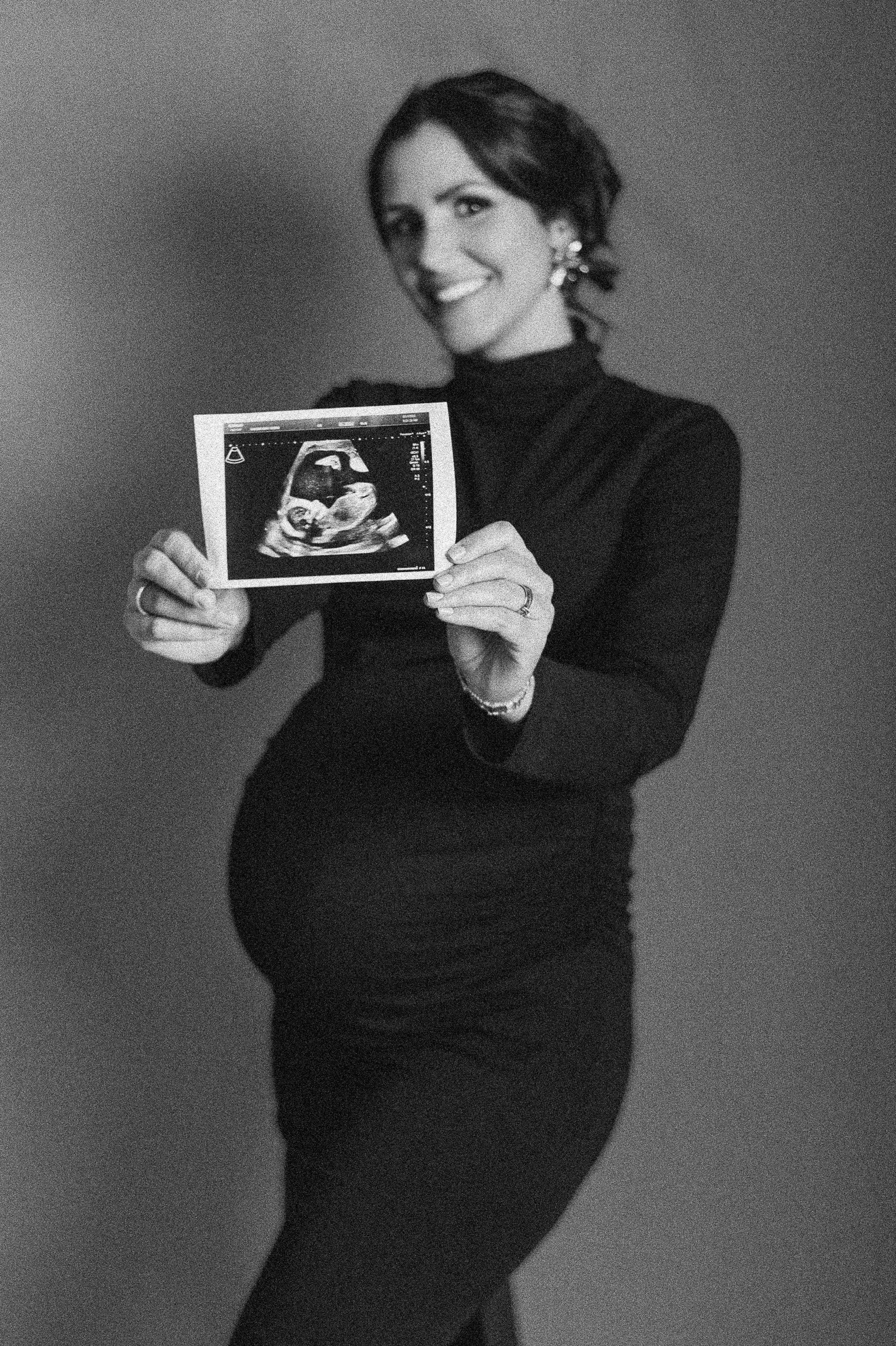 Person in black sweater holds ultrasound photos in black and white portrait series.