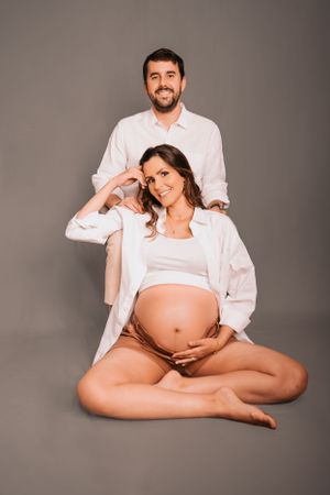 Light and airy maternity photos with couple in white clothing on gray backdrop.