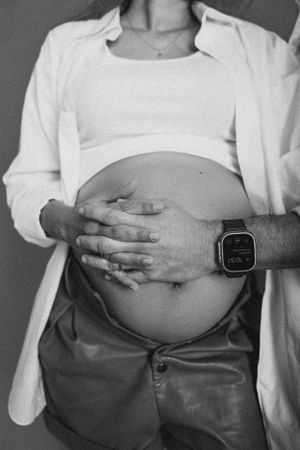 A black and white photo showing a pregnant belly with hands wearing a smartwatch resting on it.