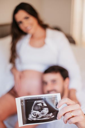 A pregnancy photo with an ultrasound image being held up in the foreground.