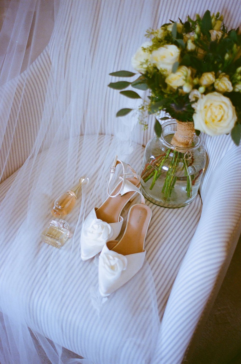 White bridal shoes and floral arrangements displayed on a striped fabric background.