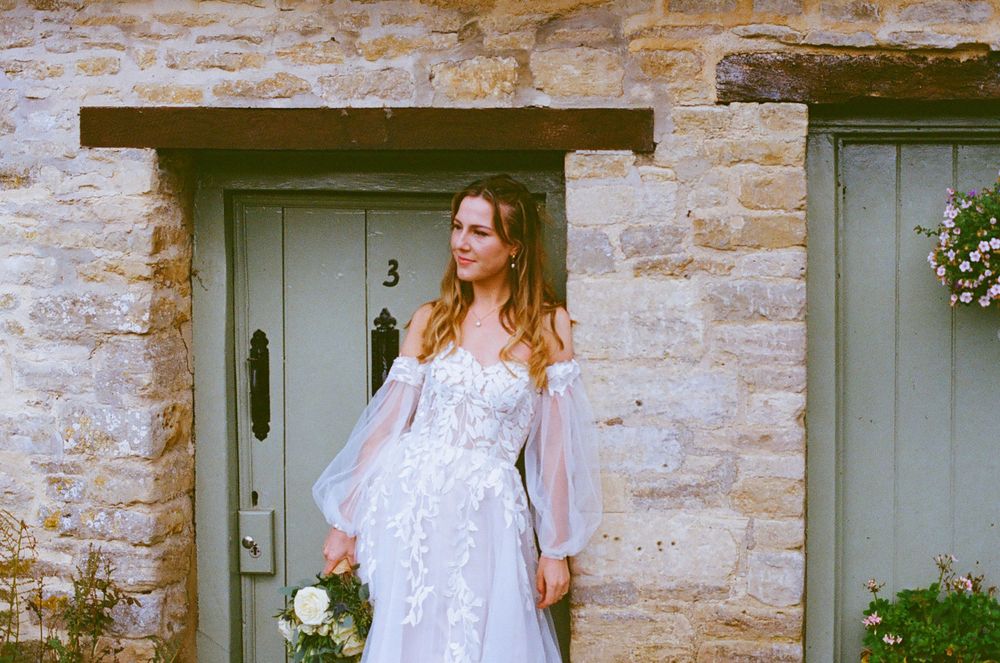 White lace dress photographed against a rustic stone wall with green doors.