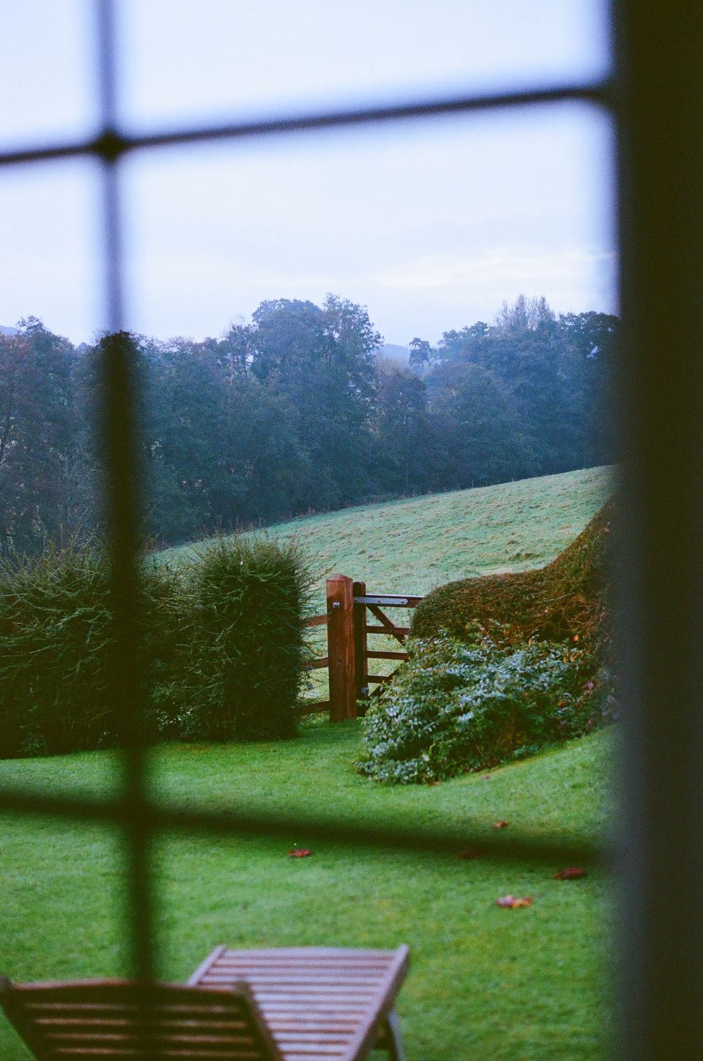 A serene countryside landscape with rolling hills and wooden fence viewed through a window.